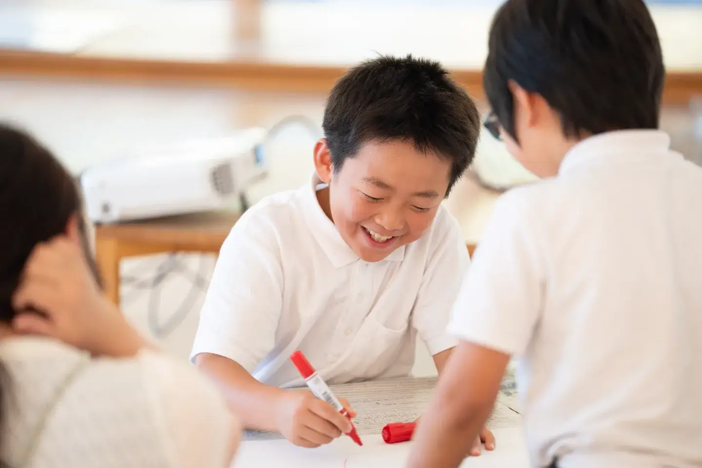 赤いペンを握り、笑顔で意見を書き出す小学生